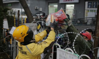 Un rider ritira un ordine da un supermercato di Pechino epa08258382 A food delivery man (L) gets food from a supermarket staff member from across a barbed wire fence set up along a residential compound blocking off entrances and paths to not allow non-local residents entry, as a means of preventing coronavirus infection, in Beijing, China, 29 February 2020. Daily life in Beijing has been affected by the COVID-19 coronavirus outbreak. EPA/WU HONG